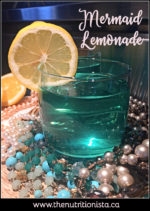 A pretty turquoise lemonade in a clear glass garnished with a lemon ring and surrounded by mermaid-inspired pearls and turquoise/aqua beads.