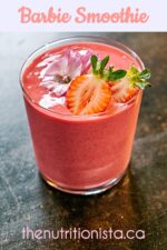 Pretty pink smoothie in a clear glass garnished with cut strawberries and a purple edible flower.